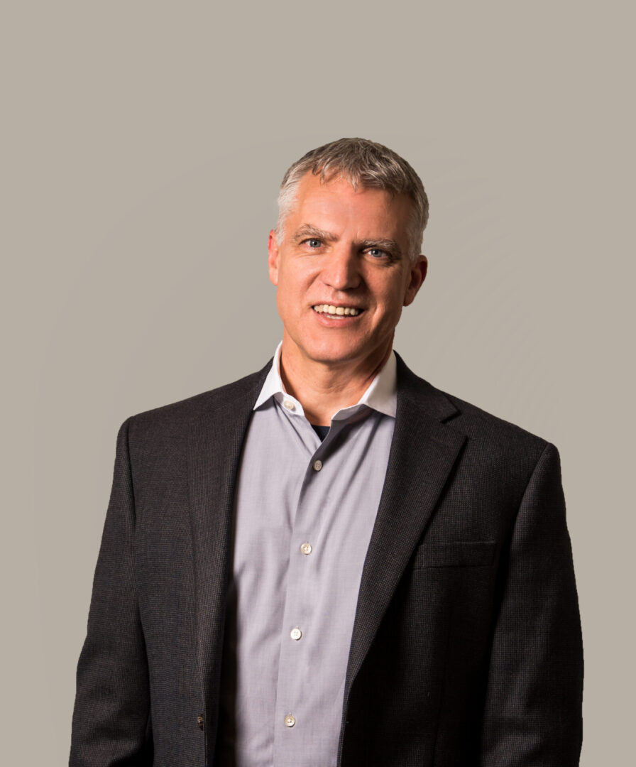 A picture of a gray-haired man wearing a button-up shirt with a black suit jacket